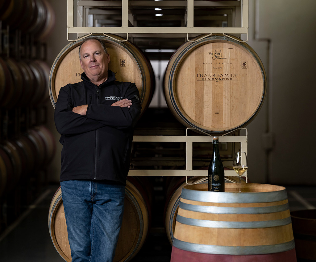 Todd Graff folds his arms and smiles next to a barrels of wine