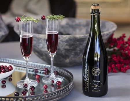 A bottle of Sparkling Rouge with two wine glasses and cranberry garnishes