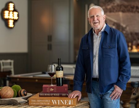 Rich Frank stands next to a pile of books with a wine bottle and wine glass resting on top