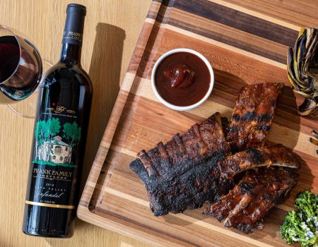 A bottle Frank Family's Zinfandel next to a cutting board with grilled ribs and BBQ sauce