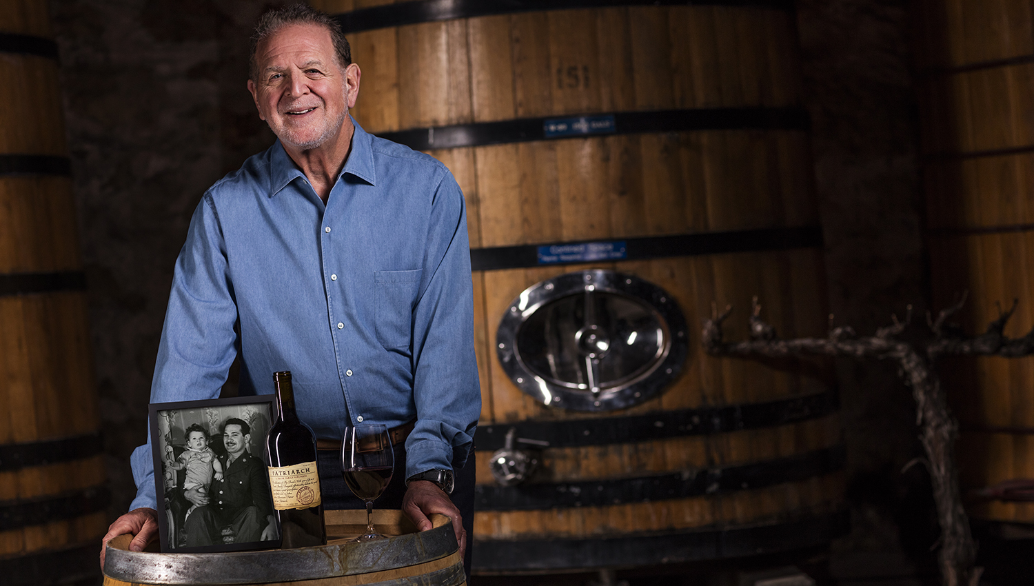 Rich poses in front of a wooden fermenter with a picture of Hy Frank sitting on top of a wine barrel