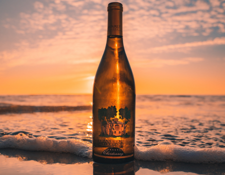A bottle of Frank Family Carneros Chardonnay on the beach at sunset