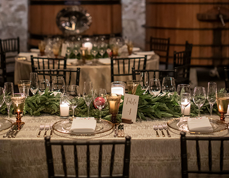 A long festive dinner table set with wine glasses, gold plates, and a pine garland